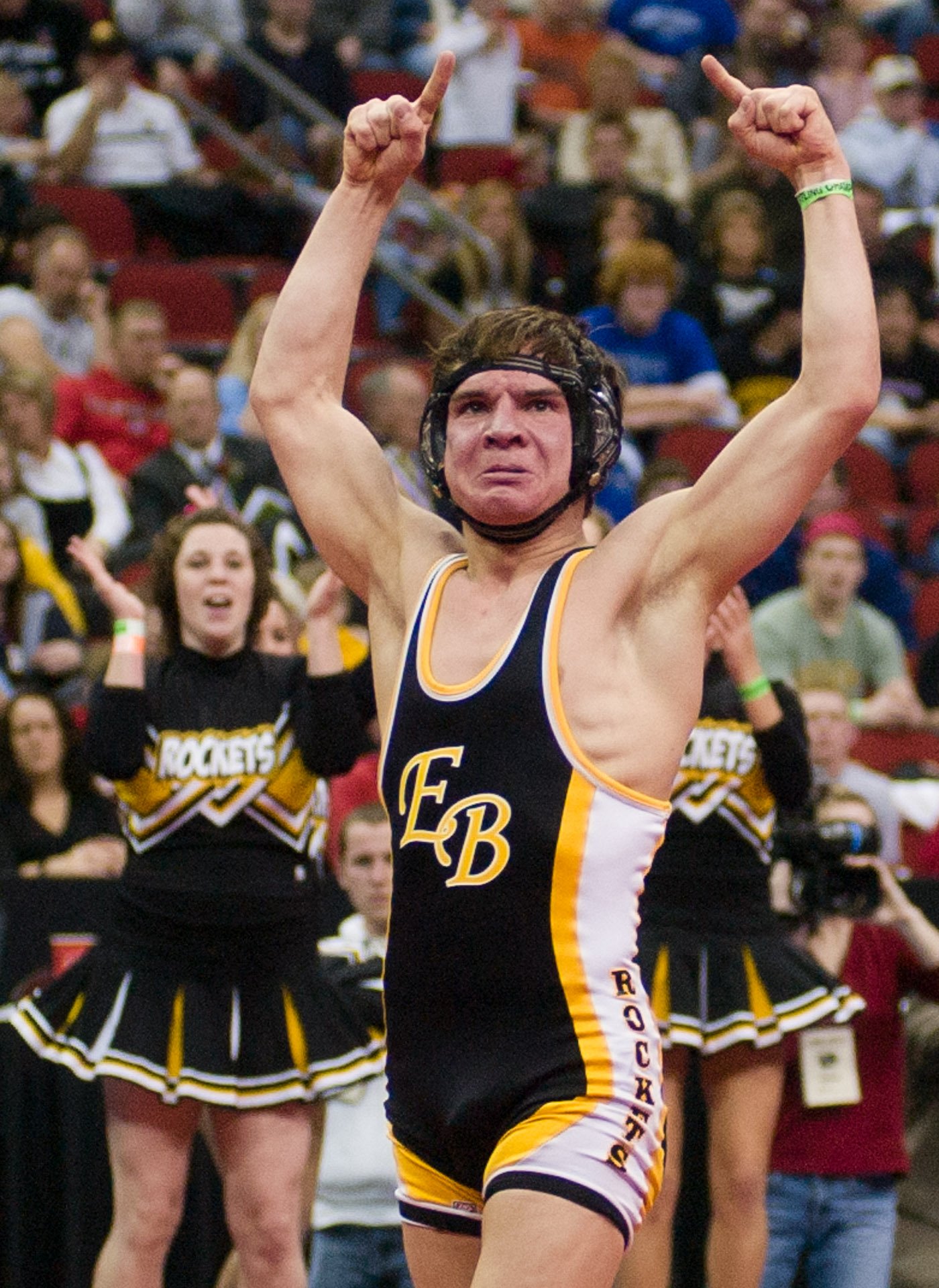 Wrestler holding hands in the air after defeating an opponent at the state tournament.
